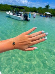 a woman's hand with white nails is in the water next to a boat