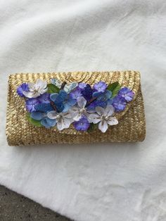 "Beautiful handcrafted wicker clutch with-purple , white and periwinkle flowers! Item has three butterflies made from feathers-there is glitter , pearl and rhinestone details as well! This is a great conversation piece! Great beach wedding or summer party clutch!! The dimensions are 10\"by 6\" by 3\"\"!This clutch has a magnetic snap closure! Such a pretty piece, you will love this ,especially if you love pretty and feminine things! I started making these for myself to go to partys to match my outfits and my friends or someone would ask me where i got it and when they learned i made them they would ask me to make them one! So I decided to share theses with anyone who loves pretty things you cant find in the store! This listing is for the clutch ONLY, I like to have a picture of a suggested Handmade Clutch For Spring Party, Handmade Spring Party Clutch, Spring Party Straw Bag, Handmade Straw Bag For Summer Evenings, Handmade Straw Bag Perfect For Spring Gift, Handmade Straw Bag Gift For Spring, Handmade White Summer Clutch, Handmade White Clutch For Summer, Wicker Clutch