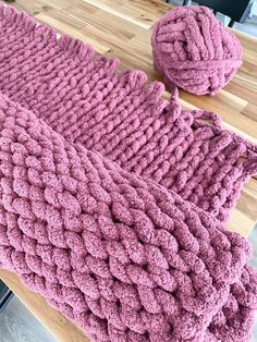 a pink knitted blanket sitting on top of a wooden table