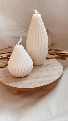 two white vases sitting on top of a wooden plate