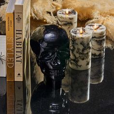 three candles sitting on top of a table next to a skull head and bookend