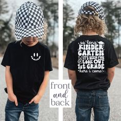 two children wearing black and white shirts with checkered hats on their heads, one is looking down at the ground