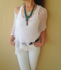 a woman standing against a wall wearing white pants and a crochet top with a green necklace