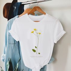 Hawkweed T-Shirt. Sustainable 100% Organic Cotton, womans Fit, Yellow flower T-Shirt. Botanical T-Shirt, Floral T-Shirt. This lovely botanical t-shirt features an original illustration by British artist Rosemary Fugeman, founder of Britain Illustrated.  DETAILS * Womens sizes XS - 3XL * Fully sustainable 100% organic cotton * Fair wear, fair trade approved * Fabric weight: 4.57 oz/yd² (155 g/m²) COLOUR * White Enquries If you have any questions please get in touch with us here at the studio. bri White Botanical Crew Neck Top, White Botanical Screen Print Tops, Botanical Cotton T-shirt For Spring, Cotton Botanical T-shirt For Spring, Botanical Crew Neck T-shirt With Screen Print, Botanical Screen Print Crew Neck T-shirt, White Botanical Graphic Print T-shirt, Yellow Crew Neck T-shirt With Plant Print, Birth Flower Short Sleeve T-shirt For Summer