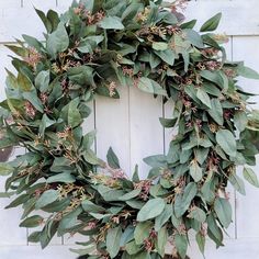 a wreath is hanging on the side of a white door with green leaves and pink flowers