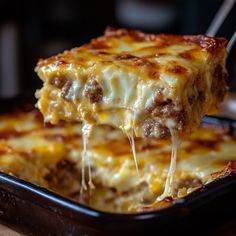 a piece of lasagna being lifted from a casserole dish with cheese