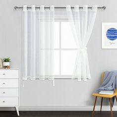 a white chair sitting next to a window in a room with a painting on the wall