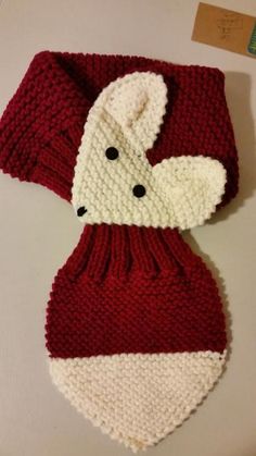 a red and white knitted scarf on top of a table next to a tag