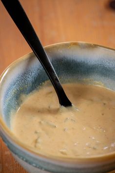 a spoon in a bowl on top of a wooden table next to a cup filled with liquid