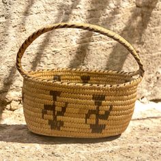 a woven basket sitting on the ground next to a stone wall with shadow from it