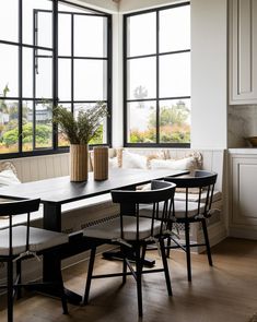 a dining room table with four chairs and a bench in front of large open windows