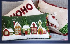 two christmas pillows sitting on top of a couch next to each other with houses and trees