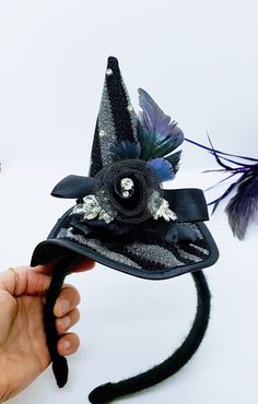 This Witch Hat Fascinator is an easy and classy way to dress up this year! This is a black and silver witch hat that is attached to a black yarn wrapped headband. The hat is adorned with ruffled lace, a netted flower, rhinestones and iridescent feathers. Will Fit a 4 year old and up! Like our Facebook Page and get 10% off when you message me before checkout! Everything made by handmade MKE is one of a kind and unique, however, if you would like a different size or see a piece that you would like Curved Brim Costume Hats And Headpieces, Halloween Novelty Wide Brim Costume Hat, Halloween Novelty Costume Hat With Wide Brim, Novelty Wide Brim Halloween Costume Hat, Brimmed Costume Hats And Headpieces, Novelty Brimmed Costume Accessories For Costume Party, Halloween Novelty Costume Accessories With Curved Brim, Novelty Brimmed Mini Hats For Costume Party, Novelty Brimmed Mini Hats For Costume