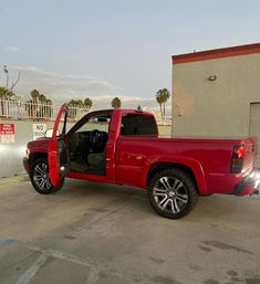 a red pick up truck parked in front of a building with its doors open and the door ajar