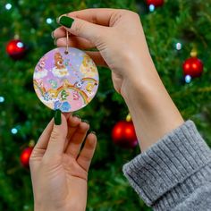 a person holding up a christmas ornament in front of a tree with lights