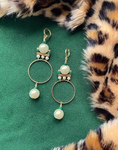 These gorgeous and unique statement hoops were designed in the art deco style of the 1920's. These are the perfect earrings for dressing up your holiday attire.These hoop earrings hang approximately 3.5" from the lobe and measure approximately 1.25" inches at their widest point. The design contains 12mm faux pearls, 4mm faux pearls, 3mm malachite heishi beads, and gold plated brass components.The leverback closure is 22k gold plated and should be suitable for sensitive ears. These are semi-light Retro Beaded Dangle Jewelry, Adjustable Retro Drop Earrings, Retro Adjustable Drop Earrings, Brass Clip-on Hoop Jewelry, Clip-on Brass Hoop Jewelry, Bohemian Clip-on Jewelry For Parties, Handmade Retro Dangle Jewelry, Retro Handmade Dangle Jewelry, Retro Brass Jewelry With Matching Earrings