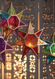 multicolored stained glass stars hanging from chains in front of a wall with lights