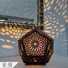 a decorative lantern sitting on top of a white table next to a mirror with the sun shining through it