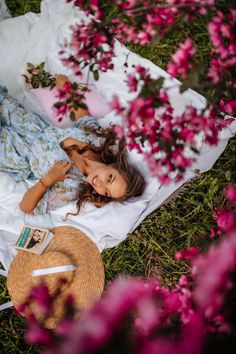 a woman laying on top of a white blanket next to a hat and flowers in the grass