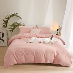 a bed with pink comforter and pillows in a room next to a potted plant