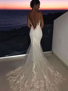 a woman in a wedding dress looking out over the ocean at sunset with her back to the camera