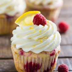 a cupcake with white frosting and raspberries on top is sitting on a wooden table