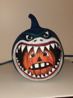 a painted pumpkin with a shark's mouth and teeth on the front, sitting on top of a table