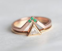 a close up of a ring on a white surface with a diamond and emerald in the middle