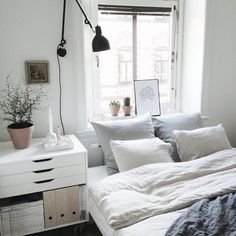 a bed with white sheets and pillows next to a window in a room that has a lamp on the wall