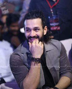 a man with a beard smiles while sitting in front of other people at an event