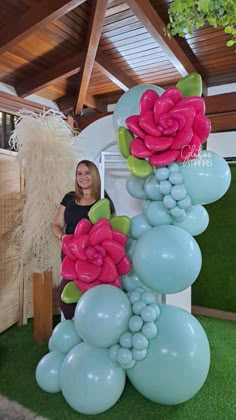 a woman standing next to a tall balloon sculpture with flowers on it's side