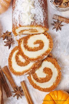 cinnamon roll with icing sitting on top of white paper next to spices and pumpkins