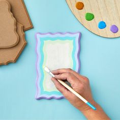 a person using a paintbrush to decorate a paper card with shapes and colors on it