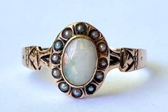 "Very pretty opal and natural seed pearl ring from the Victorian era in 10K yellow gold. This lovely ring features an oval opal cabochon with a halo of white seed pearls. The top of the ring measures 9.6mm north to south, andm the opal measures 6.4x4.4mm. The center opal glass has beautiful fire. Ring size 5 3/4 and easily sized up or down several sizes. Ring sizing service available; please see sizing fees listed below. Please allow one week for sizing. One month layaway payment plans available on items $850 and over. Approximate Age - Victorian Gemstone(s) - opal and natural seed pearls Metal - 10K yellow gold Weight - 1.15 grams Ring size - 5 3/4  Marks -  Makers Mark -  Comments -  Service & Sizing Information: If you require ring sizing or service, kindly follow the link below to add Art Deco Oval Ring, Victorian Oval Pearl Ring With Gemstone, Victorian Oval Cabochon Pearl Ring, Victorian Oval Cabochon Moonstone Ring, White Oval Victorian Opal Ring, Victorian White Oval Opal Ring, Victorian Oval Opal Ring Hallmarked, Victorian Style Oval Opal Ring With Hallmark, Victorian Oval Opal Ring For Anniversary