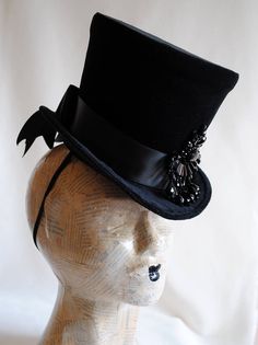 The Tease is a fabulous dark fashion lady's top hat,luxuriously elegant and feminine all the way! It is covered with rich black velvet and trimmed with black ribbon around the crown that ends in a beautiful double black bow at the back. The focal point is a majestic hand-beaded black crystal element at the side front that sparkles as you move around. Measurements : height 6.5 inches( 16 cm ) front to back 9 inches ( 23 cm ) side to side 8 inches ( 20 cm ) THIS IS NOT A FIT TO HEAD HAT NOT SUITAB Black Top Hat For Costume, Fitted Hats For Halloween Evening, Black Fitted Top Hat For Costume, Fitted Black Top Hat For Costume, Fitted Halloween Evening Hats, Fitted High Crown Hat For Costume Party, Victorian Fitted Hats For Costumes, Victorian Fitted Costume Hats, Victorian Style Fitted Costume Hats