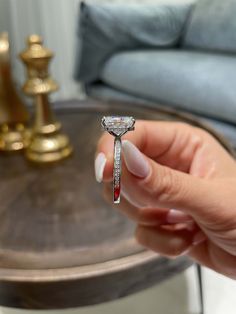 a woman holding a diamond ring on top of her finger in front of a couch