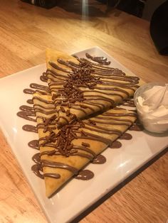 three pieces of chocolate crepe on a white plate with whipped cream and caramel drizzle