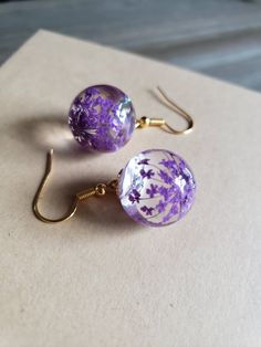 two purple and white glass bead dangles on gold earwires sitting on top of a piece of paper