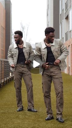 two men standing in the grass looking at their cell phones while wearing jackets and pants