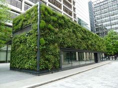 a tall building covered in green plants next to a sidewalk