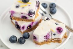 two slices of blueberry cheesecake on a white plate with silverware and fork