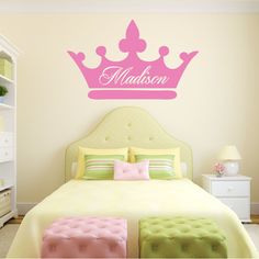 a bed room with a neatly made bed and a pink crown wall decal on the wall