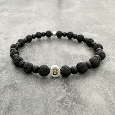 This edgy, masculine beaded bracelet for men is made of alternating lava stone and black stainless steel, with a sterling silver plated metal letter bead and stainless steel accent bead. Make this bracelet all your own by personalising with your initial or the initial of a loved one. Our 'Stone & Steel' Initial bracelet includes 7mm lava rock beads which are shaped, leaving cavities that give the stone its characteristic texture. Contrasting the textured stone with our glossy black 5mm steel bea Masculine Bracelets, Beaded Bracelet For Men, Wrist Stacks, Bracelet Initial, Metal Letter, Easy Jewelry, Metal Letters, Lava Rock, Initial Bracelet