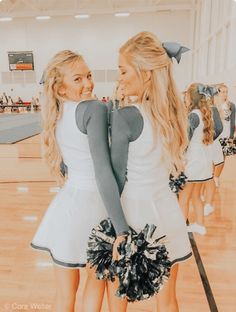 two girls in cheerleader outfits standing on a basketball court with their arms around each other