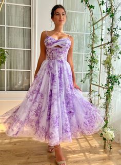 Step into the scene with this stunning lavender tulle dress, perfect for garden parties, weddings, or any special celebration. Adorned with a delicate floral print, this dress features a fitted bodice with a subtle cut-out under the bust for a hint of allure. The draped bust and cinched waist sculpt a beautiful silhouette, while the midi-length skirt offers graceful movement. Practical yet stylish, it includes inseam pockets for convenience. The lace-up back and spaghetti straps complete the loo Purple Floral Gown, Lavender Tulle Dress, Hydrangea Dress, Purple Summer Dress, Violet Sky, Teuta Matoshi, Graceful Movement, Beautiful Silhouette, Hydrangea Purple