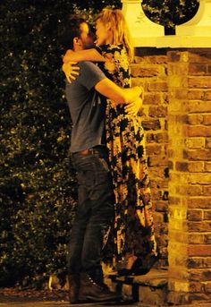 a man and woman embracing each other in front of a brick wall