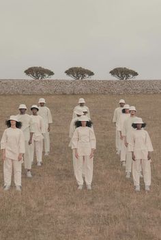 a group of people standing in a field next to each other wearing white outfits and hats