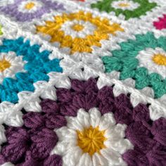 a multicolored crocheted blanket with white, yellow, purple, and green flowers