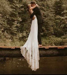 a bride and groom kissing on a bridge over a river in front of some trees