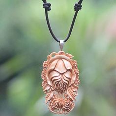 an intricately carved pendant hangs from a black cord on a green background with blurry foliage